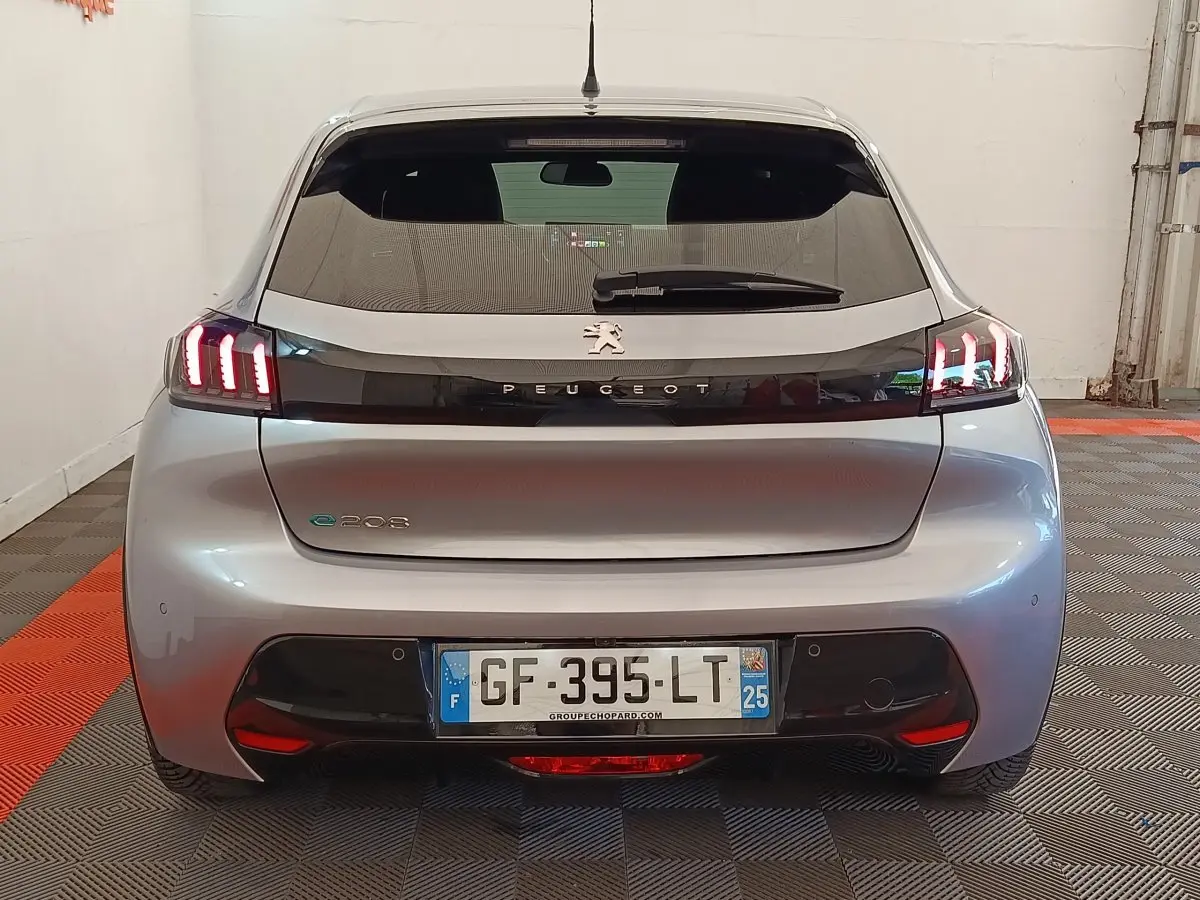 Vue arrière d'une Peugeot 208 électrique gris clair avec feux LED caractéristiques allumés en intérieur.