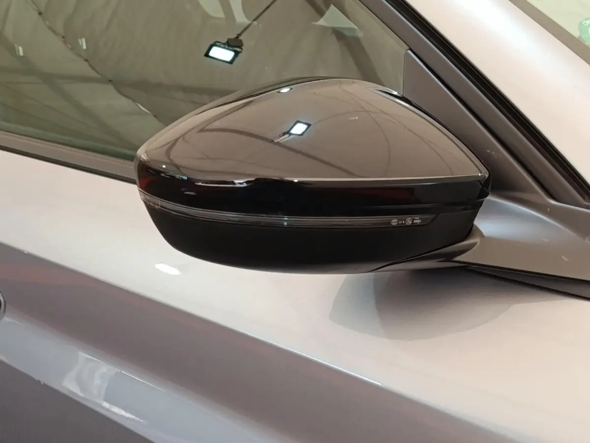 Rétroviseur noir côté gauche sur Peugeot 208 électrique gris clair, vue rapprochée en intérieur.