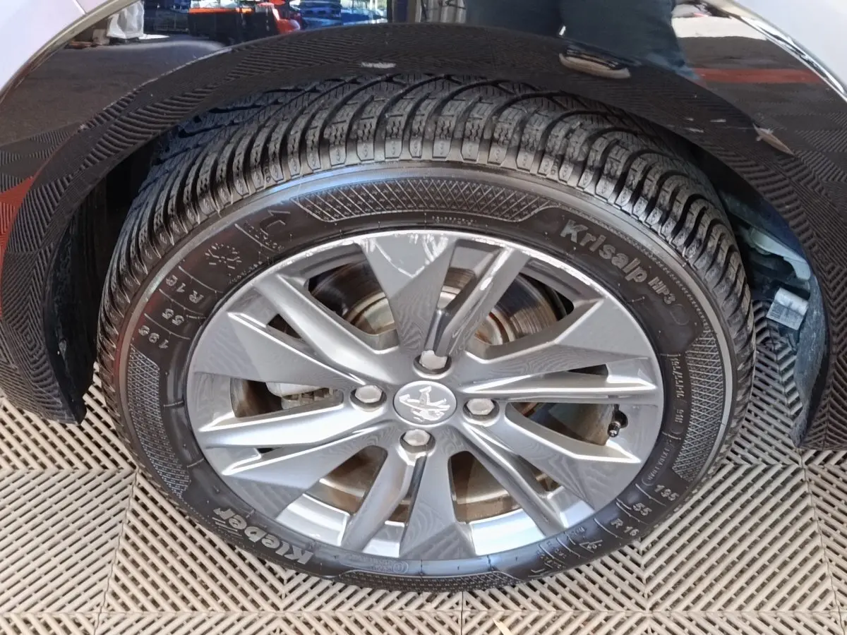 Gros plan sur la roue avant droite d'une Peugeot 208 électrique gris clair avec jante alliage à cinq branches.