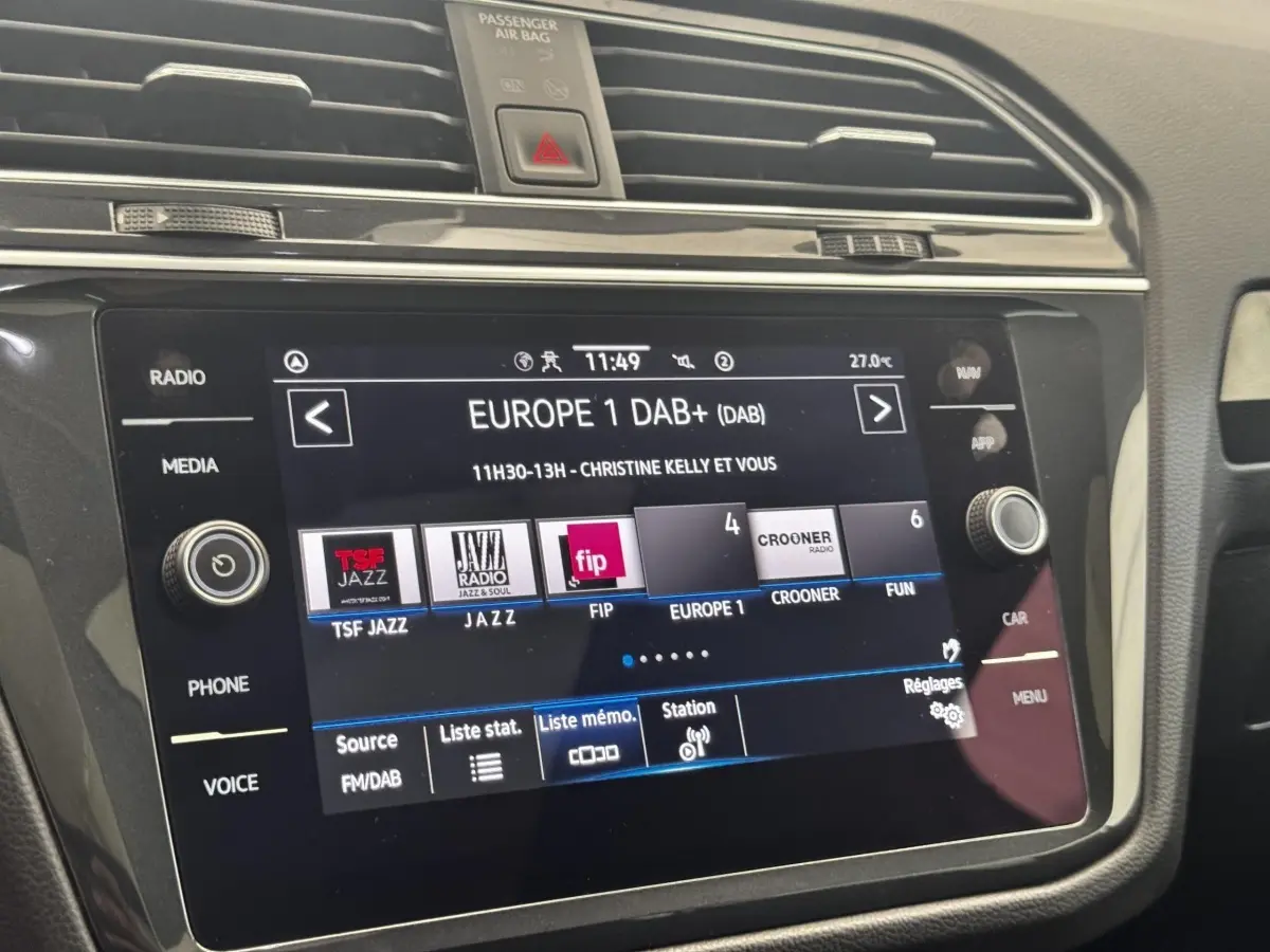 Gros plan sur l’écran tactile central du Volkswagen Tiguan 1.5 TSI gris clair affichant les stations radio DAB+ en intérieur.