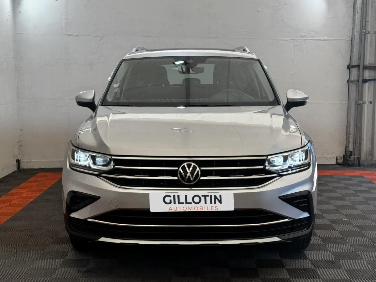 Vue avant d'un Volkswagen Tiguan gris clair avec phares LED allumés et calandre chromée dans un garage.