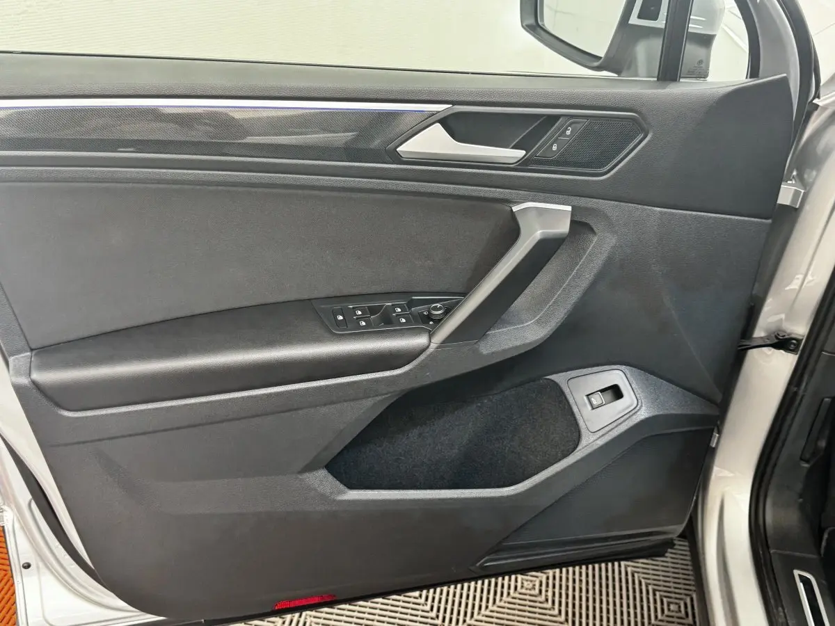 Vue rapprochée de la porte avant gauche gris clair du Volkswagen Tiguan 2021 avec commandes de vitres et poignée argentée.