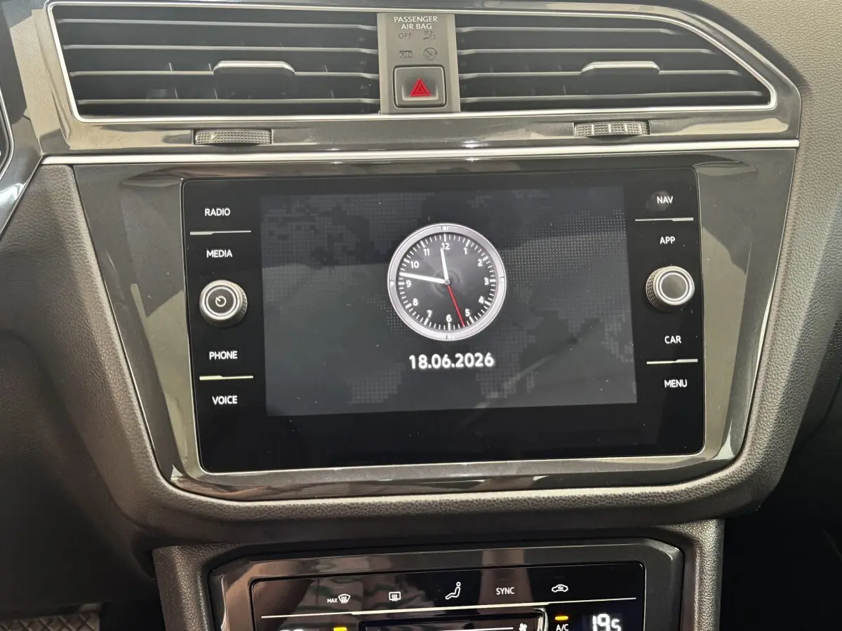 Gros plan sur l’écran tactile central noir du tableau de bord du Volkswagen Tiguan avec horloge digitale affichée.