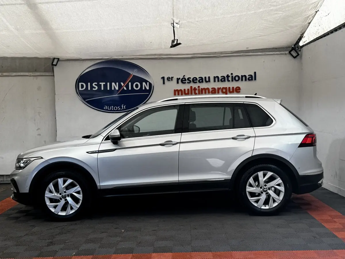 Vue latérale droite d'un Volkswagen Tiguan gris clair 2021, avec jantes alliage et barres de toit chromées visibles.