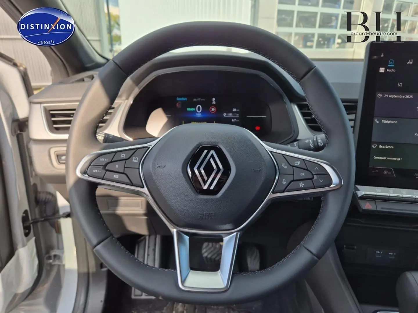 Vue rapprochée du volant multifonction noir avec logo Renault au centre, tableau de bord numérique et écran tactile à droite.