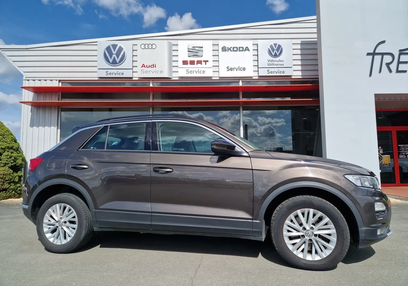 Volkswagen T-Roc chêne noir vu de profil côté gauche, avec jantes alliage et carrosserie compacte devant un garage.