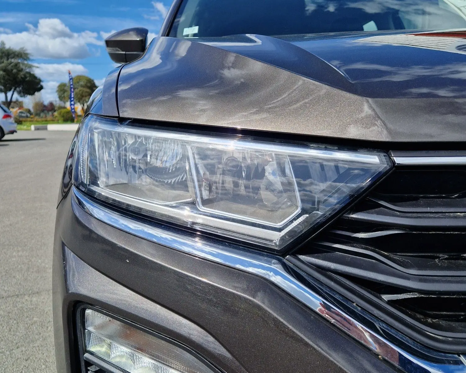 Gros plan sur le phare avant gauche du Volkswagen T-Roc Chêne Noir, soulignant ses feux LED et la calandre noire brillante.