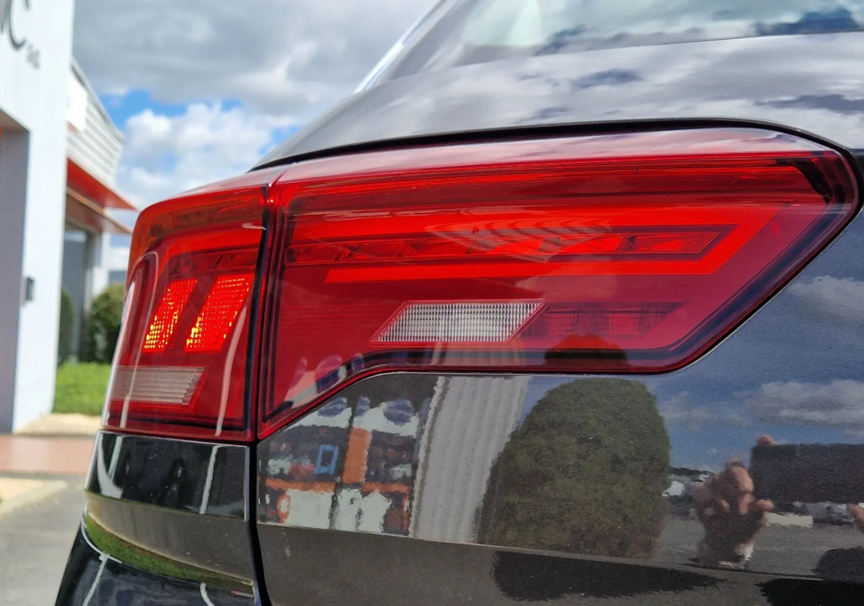 Gros plan sur le feu arrière gauche rouge du Volkswagen T-Roc Chêne Noir, reflétant l'environnement extérieur.