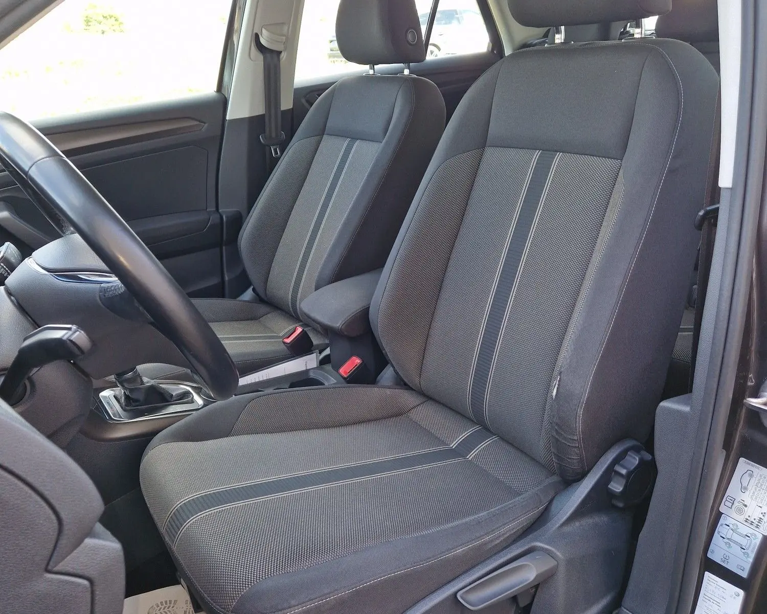 Vue intérieure côté conducteur du Volkswagen T-Roc chêne noir, mettant en valeur les sièges avant en tissu gris à rayures.