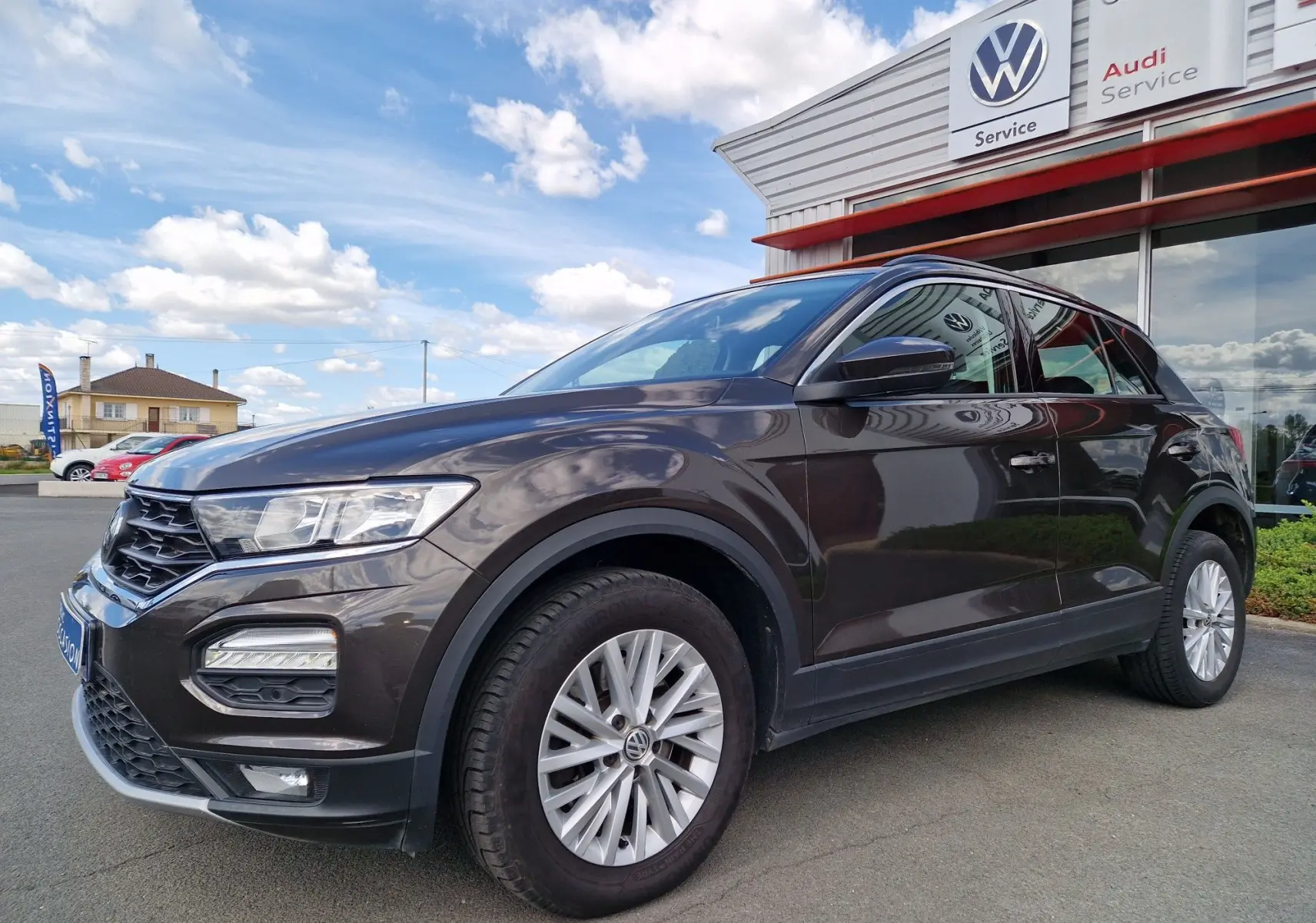 Volkswagen T-Roc chêne noir vu de 3/4 avant droit, avec jantes alliage et calandre noire brillante devant un service Volkswagen.