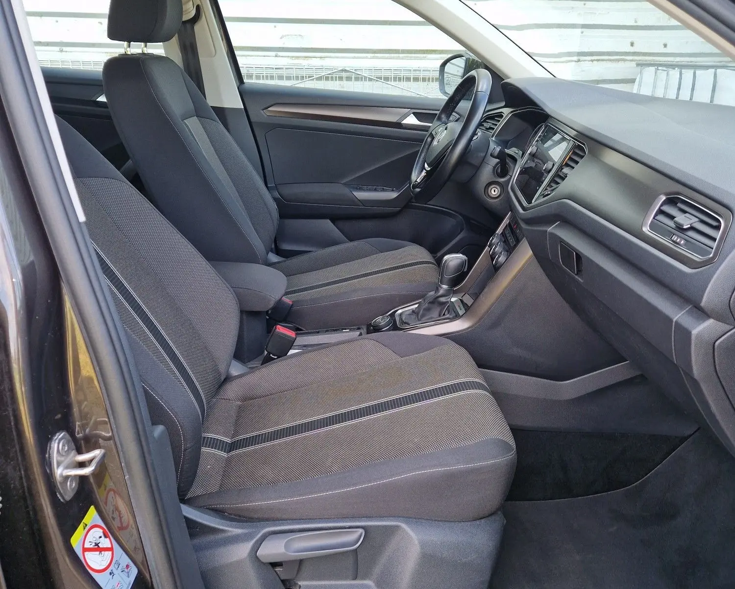 Vue intérieure côté conducteur du Volkswagen T-Roc chêne noir, montrant sièges avant et tableau de bord moderne.