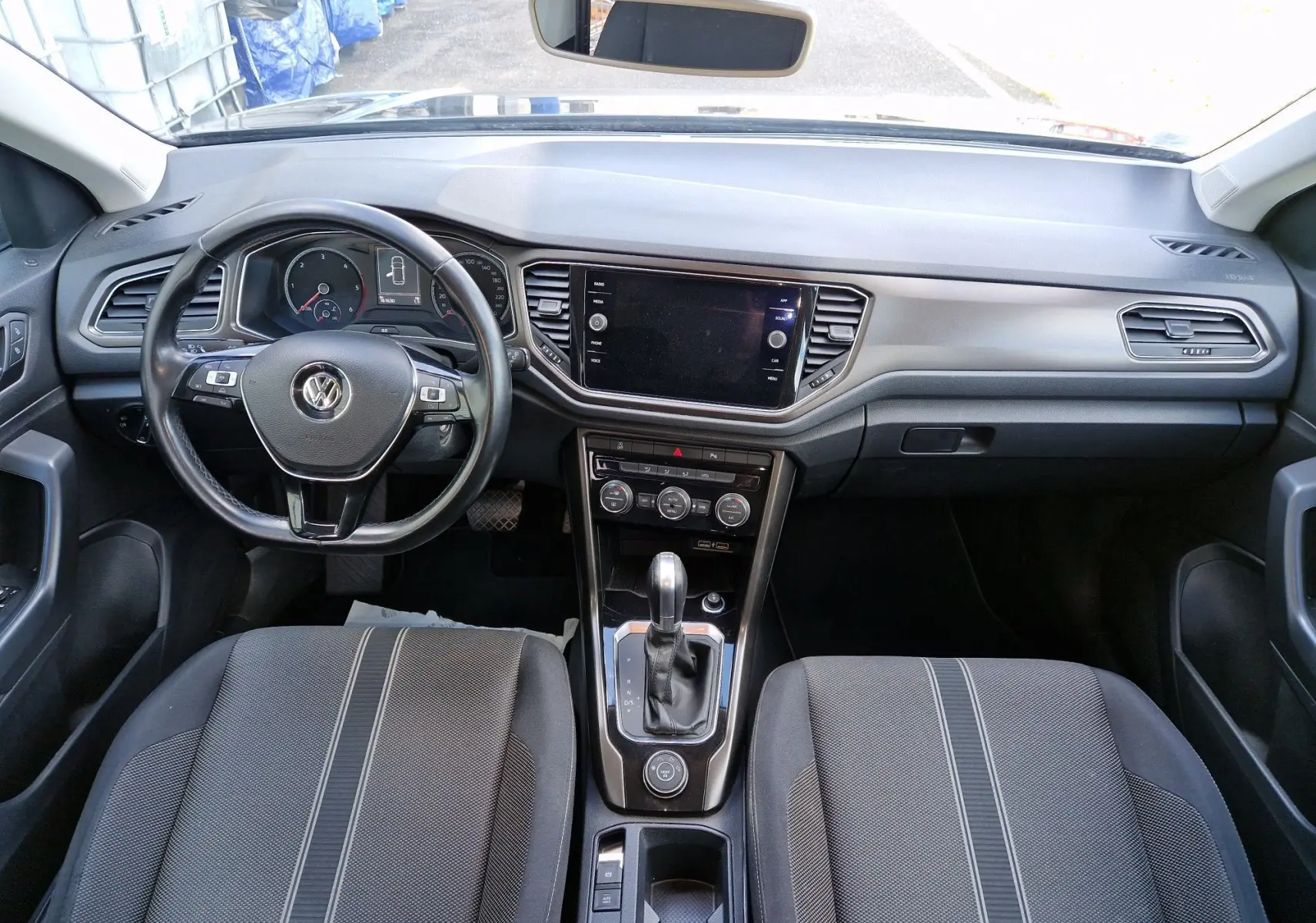 Vue intérieure avant du Volkswagen T-Roc 2.0 TDi Lounge, tableau de bord moderne avec écran tactile et volant multifonction noir.