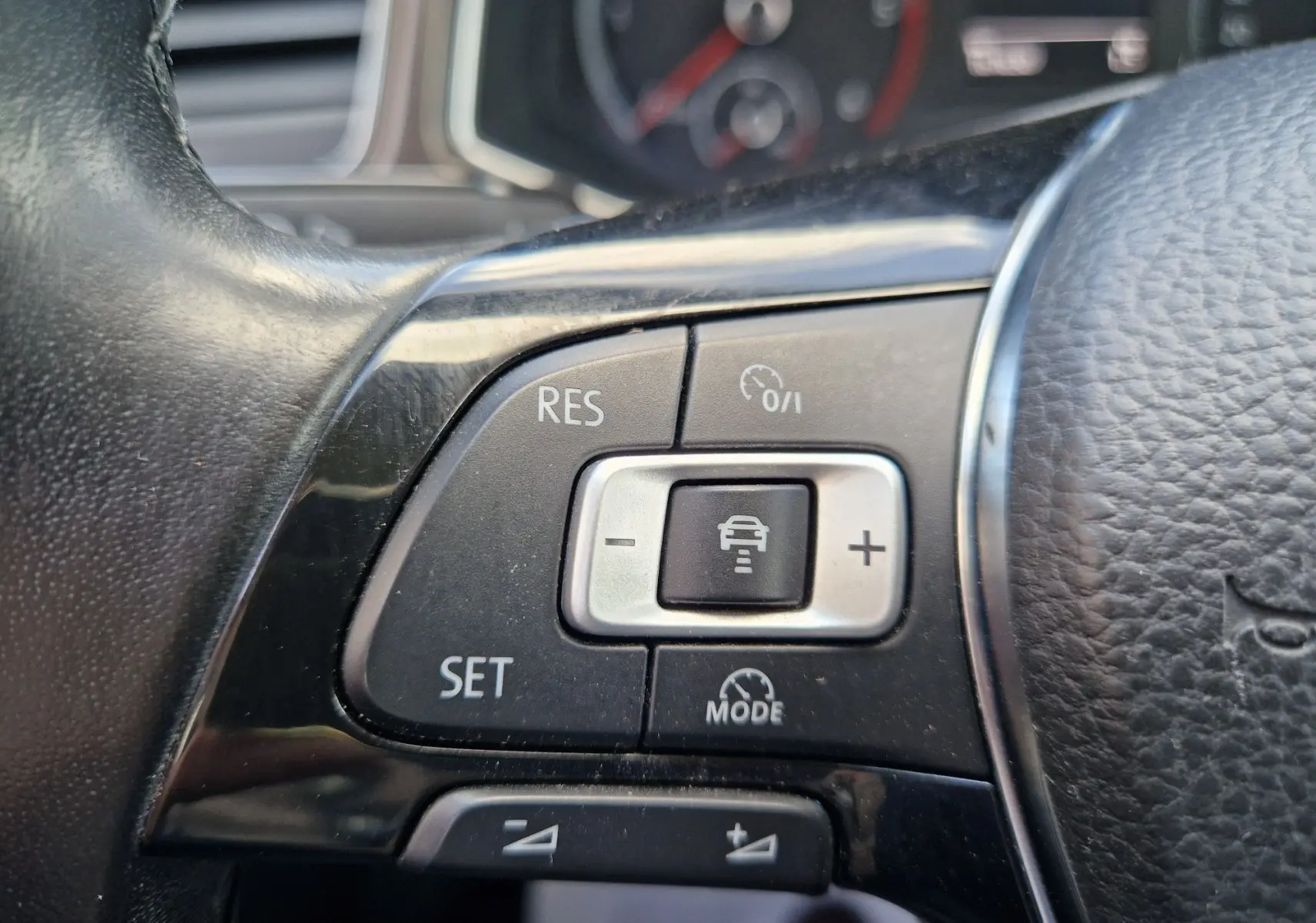 Gros plan sur les commandes du régulateur de vitesse au volant cuir d'un Volkswagen T-Roc Chêne Noir, tableau de bord en arrière-plan flou.