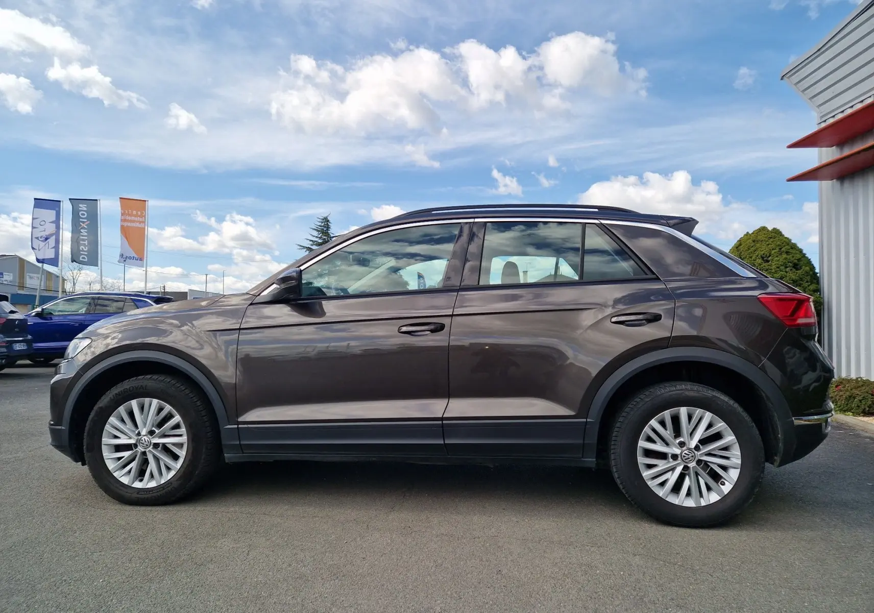Vue de profil côté gauche d'un Volkswagen T-Roc chêne noir avec jantes alliage et toit noir, stationné en extérieur.