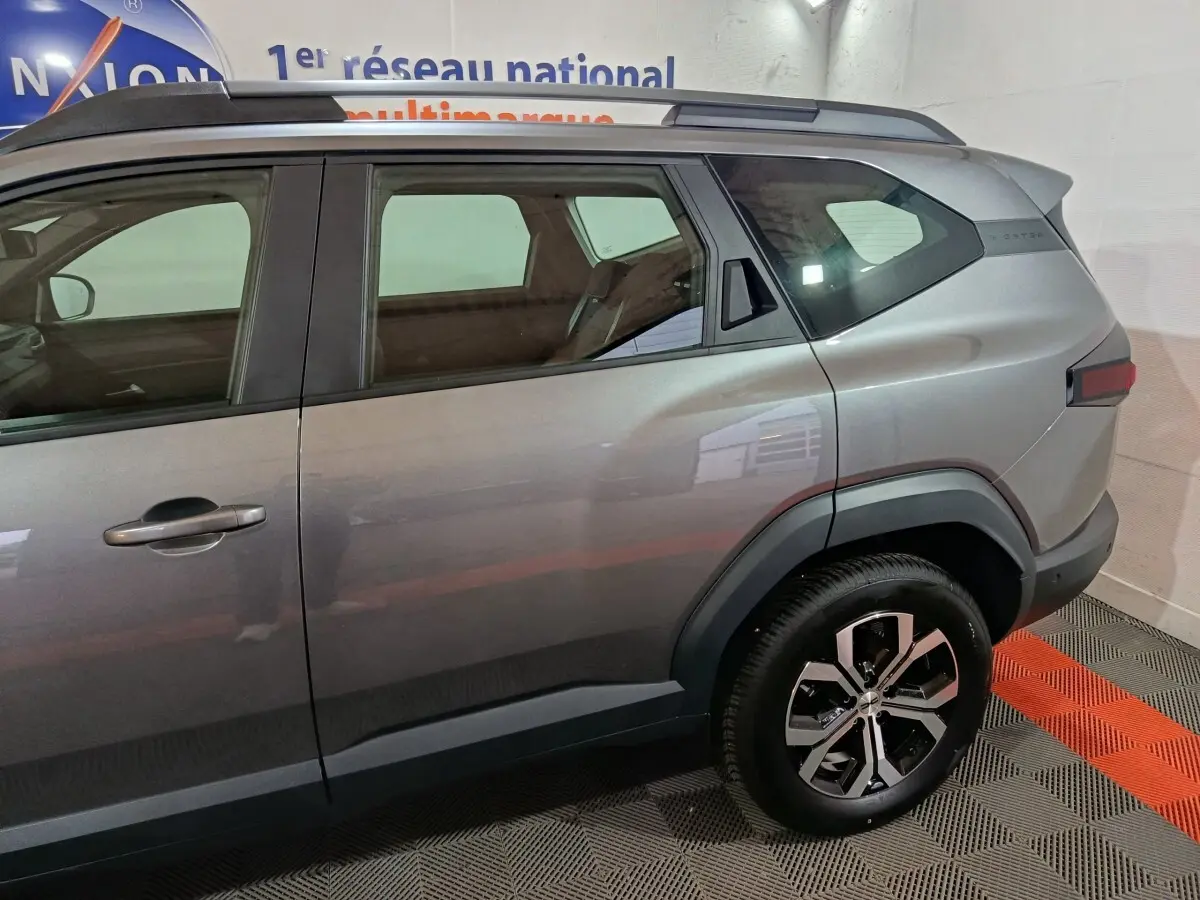 Vue latérale droite du Dacia Bigster gris foncé 2025 avec jantes alliage et barres de toit visibles.