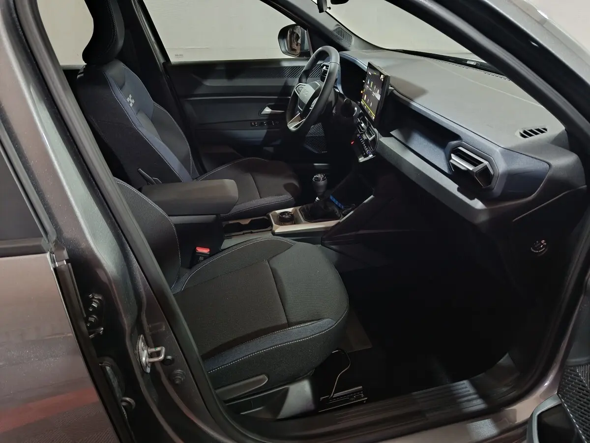Vue intérieure côté conducteur du Dacia Bigster gris foncé, montrant les sièges, le volant et l'écran tactile central.