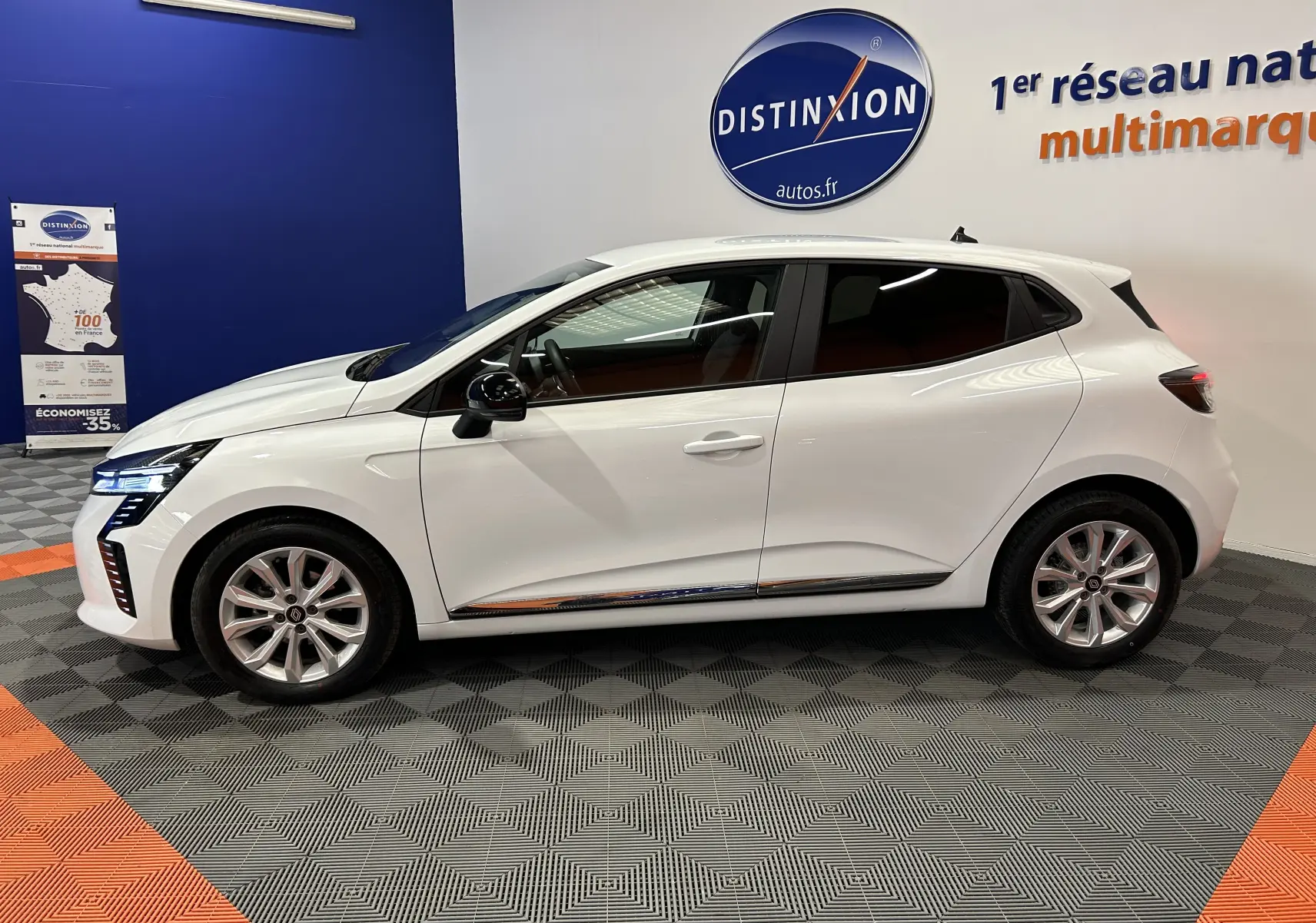 Profil côté gauche de la Renault Clio V blanche 5 portes, avec jantes alliage et vitres teintées, en intérieur showroom.