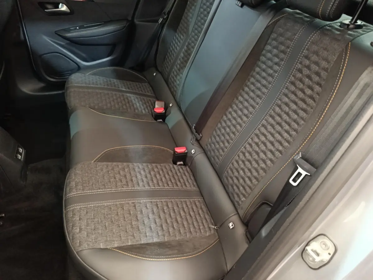 Vue intérieure de la banquette arrière en tissu et cuir noir avec surpiqûres orange d'une Peugeot 208 Electrique gris clair.