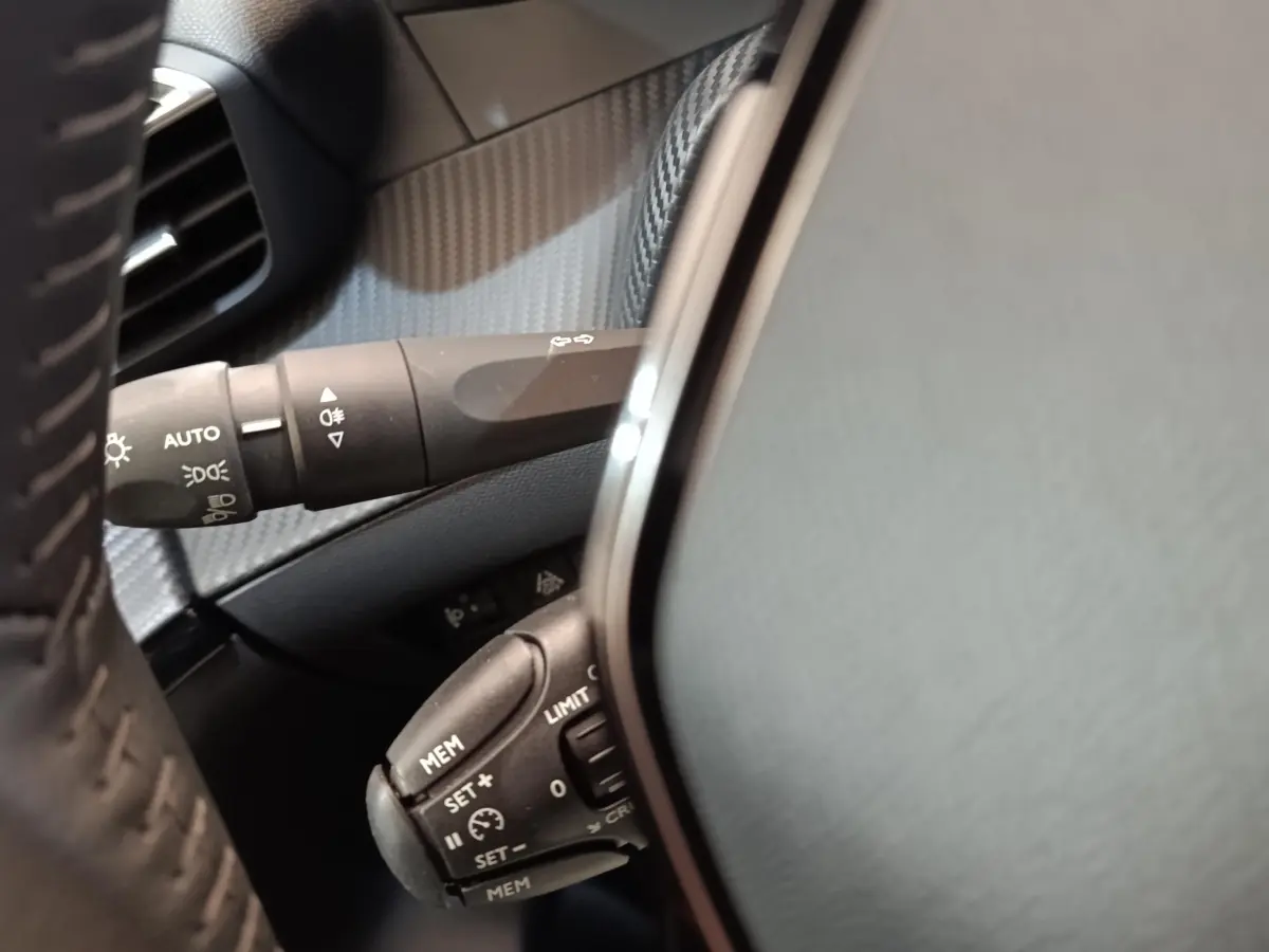 Gros plan sur les commandes au volant côté gauche du Peugeot 208 Electrique gris clair, avec réglages du régulateur de vitesse.