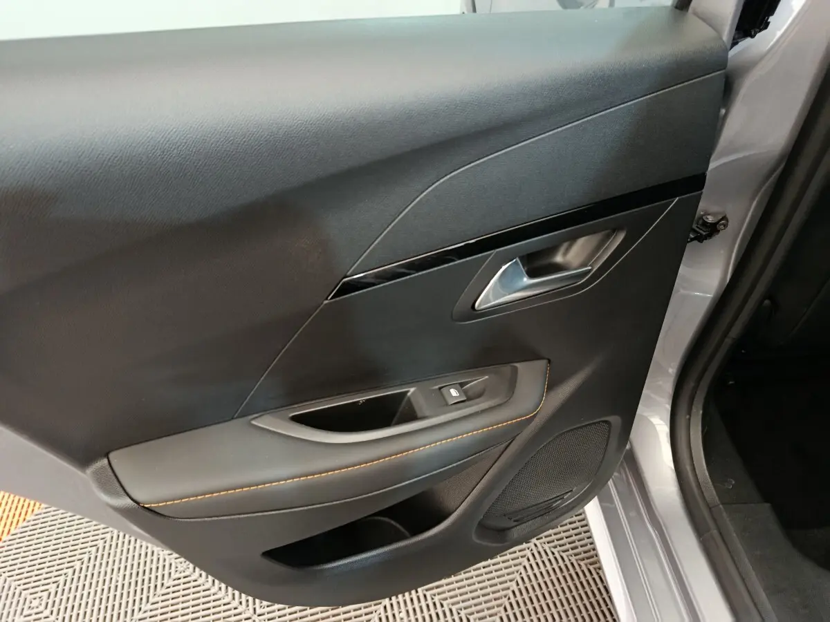 Vue rapprochée de la porte arrière droite gris clair du Peugeot 208 Electrique ROADTRIP avec poignée argentée et surpiqûres orange.