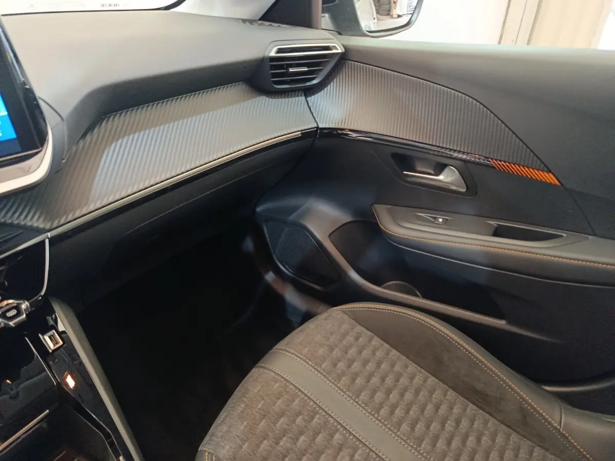 Intérieur côté passager du Peugeot 208 Electrique Roadtrip 2022, avec garnitures noires et surpiqûres orange.
