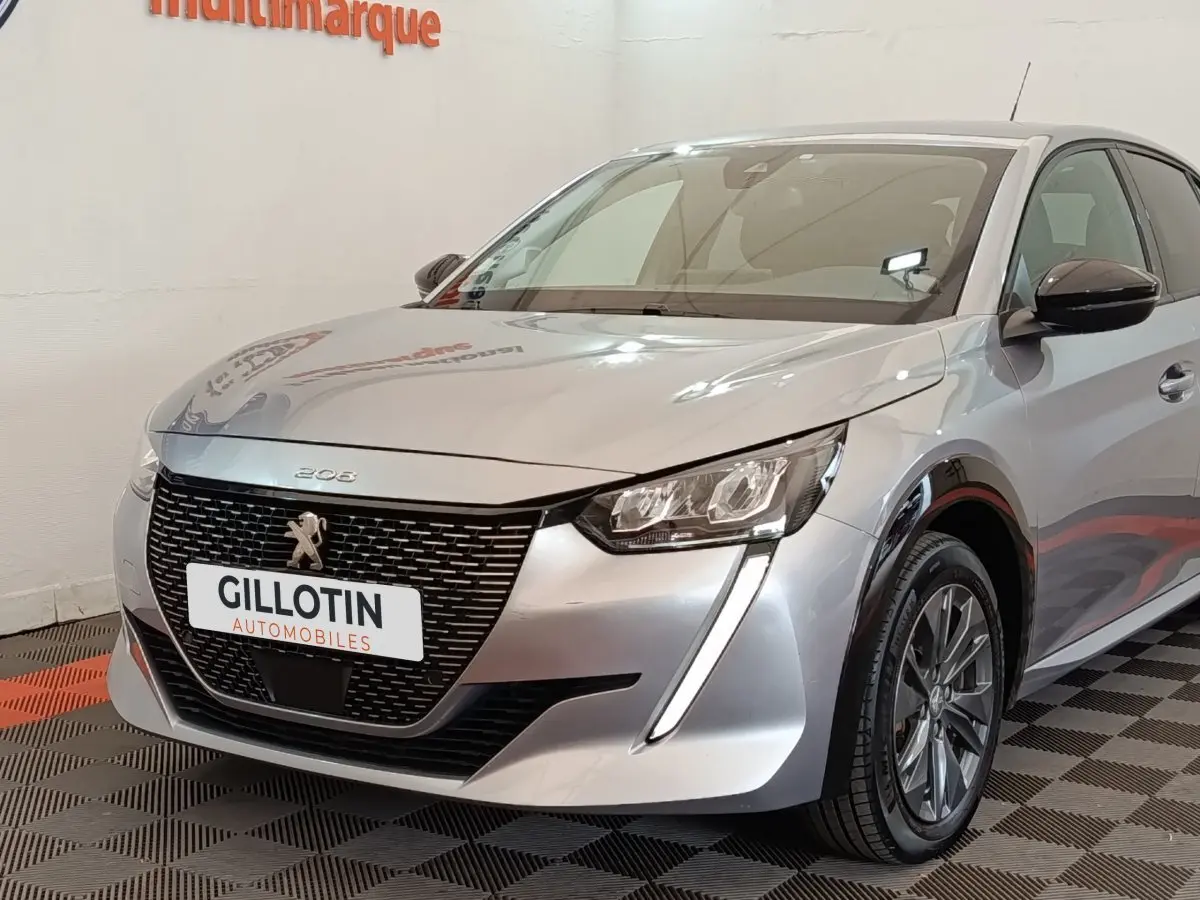 Vue 3/4 avant droit d'une Peugeot 208 électrique gris clair avec calandre noire et feux LED verticaux.