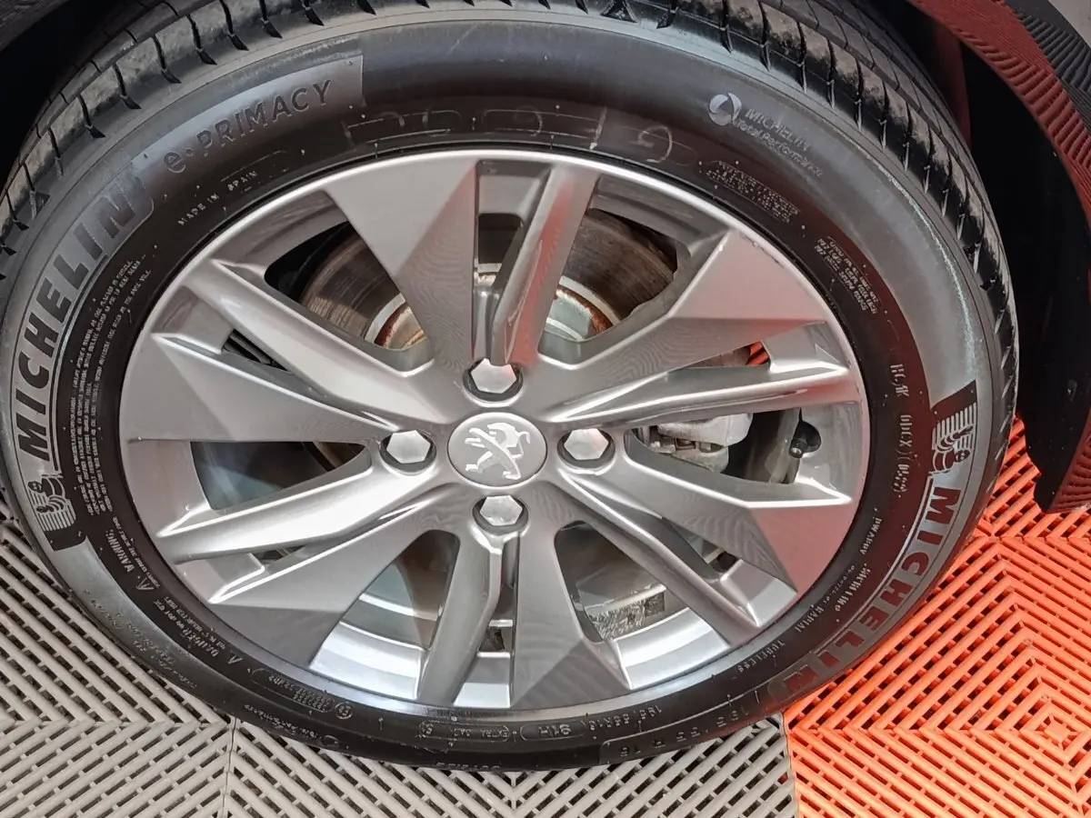 Vue de profil côté gauche d'une Peugeot 208 électrique Roadtrip gris clair sur sol rouge avec roue avant visible.