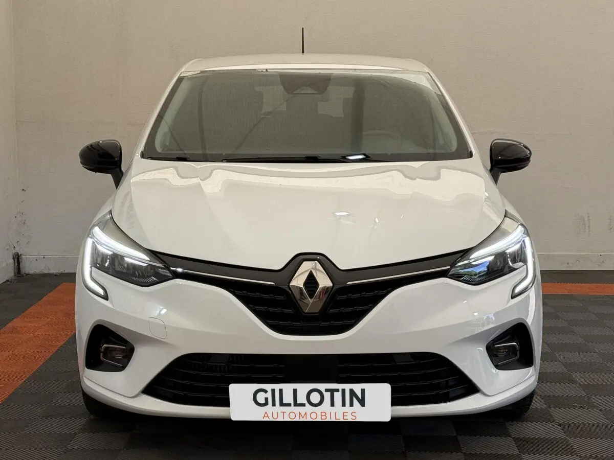 Vue frontale d'une Renault Clio Evolution TCe 100 GPL blanche avec phares LED allumés et rétroviseurs noirs.