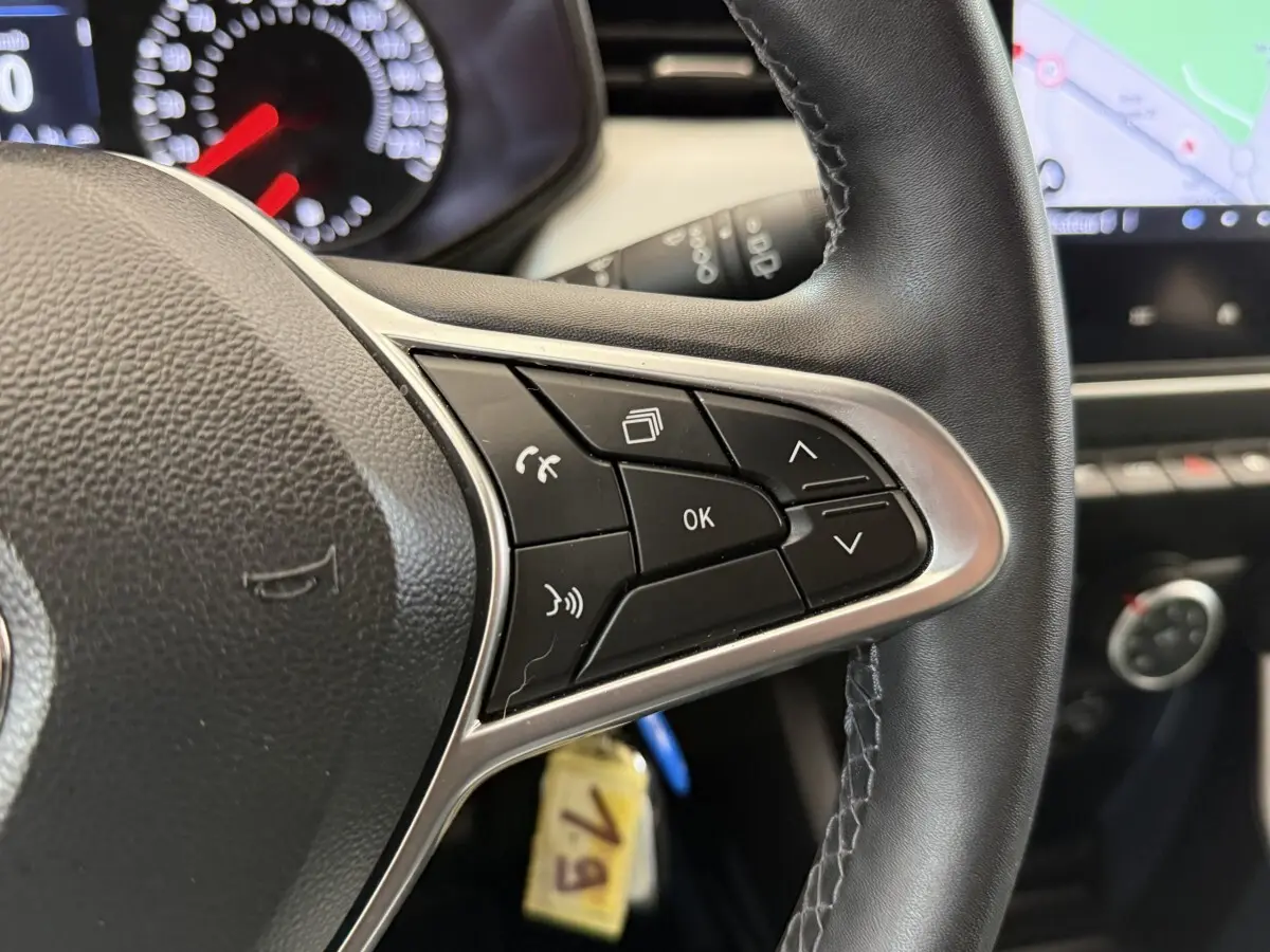 Gros plan sur le volant cuir synthétique noir de la Renault Clio 2023 avec commandes multifonctions et tableau de bord partiel.