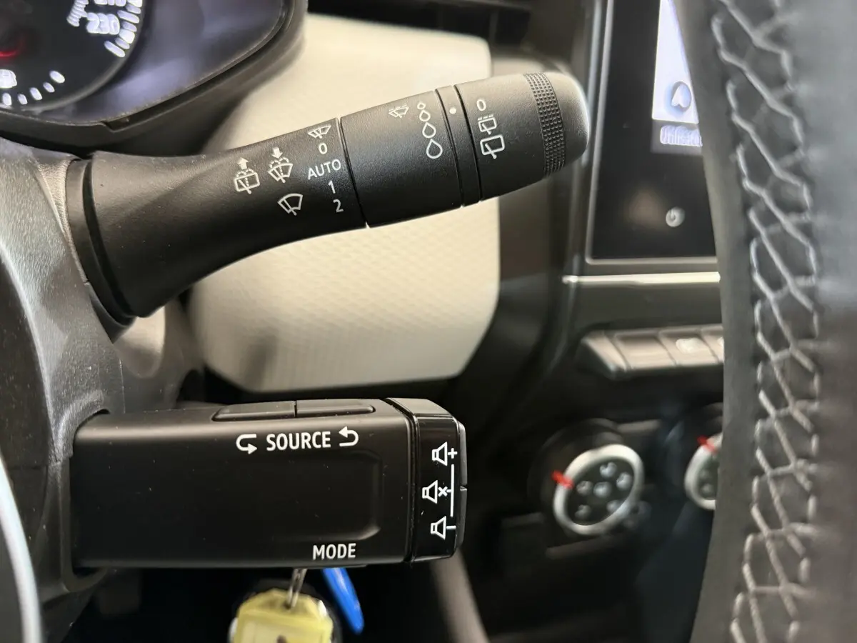 Gros plan sur les commandes au volant noir de la Renault Clio 2023, avec tableau de bord et écran tactile en arrière-plan.
