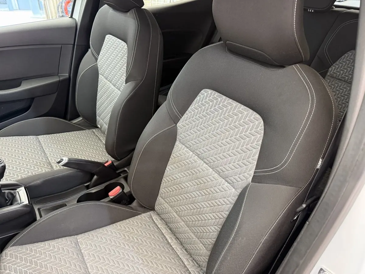 Vue intérieure côté conducteur de la Renault Clio blanche 2023, sièges tissu gris à motifs géométriques et coutures blanches.