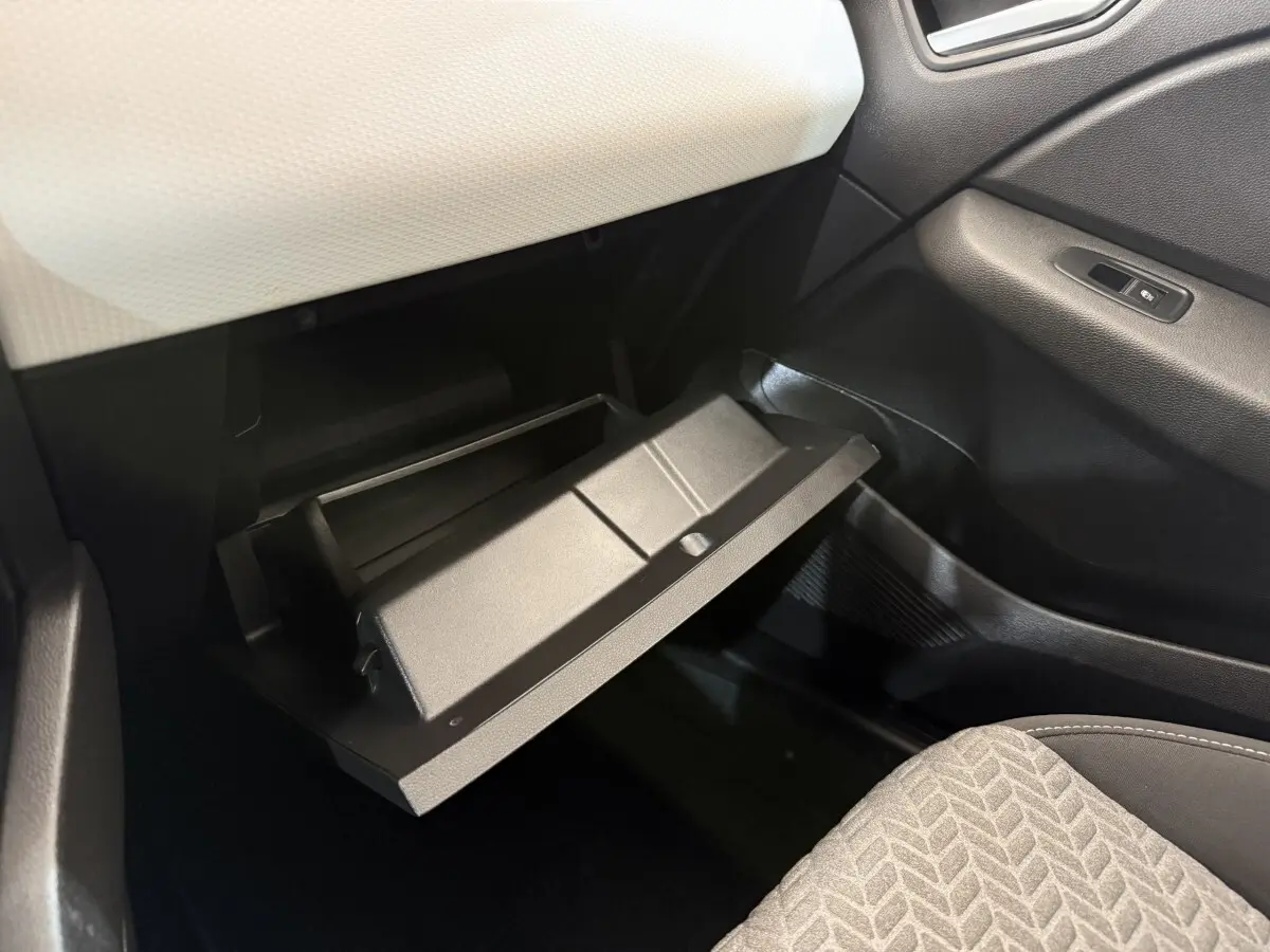 Gros plan sur la boîte à gants ouverte côté passager de la Renault Clio Evolution TCe 100 GPL 2023, intérieur noir et blanc.