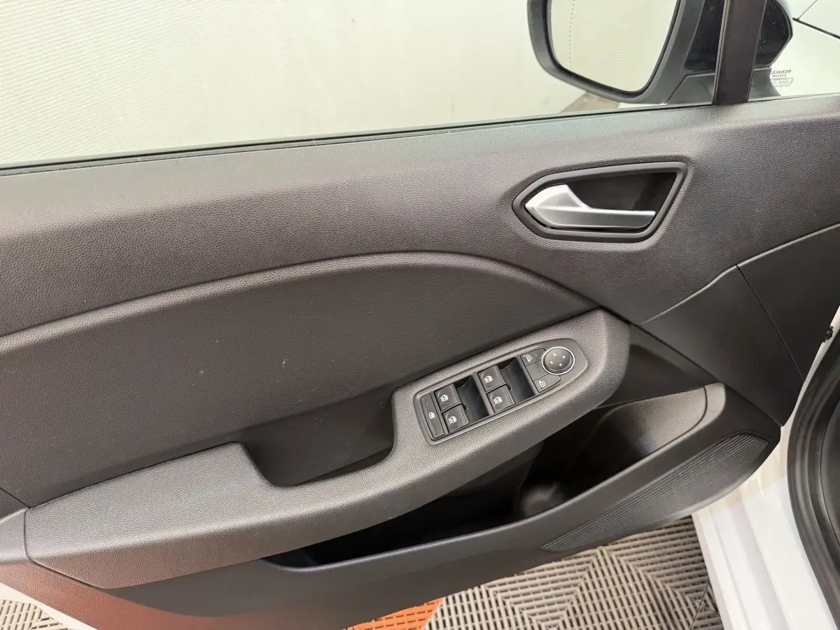 Intérieur côté conducteur de la Renault Clio blanc 2023, montrant la porte avec commandes des vitres et rétroviseur.