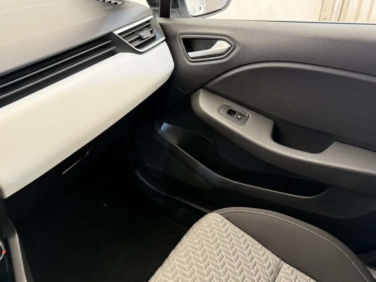 Intérieur côté passager de la Renault Clio blanc avec tableau de bord clair et porte noire, siège tissu gris à motifs.