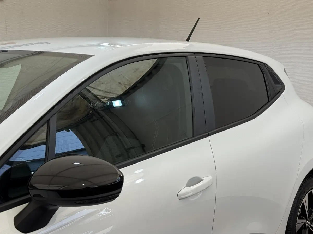 Vue latérale gauche d'une Renault Clio blanche Evolution TCe 100 GPL avec rétroviseur noir brillant et vitres teintées.