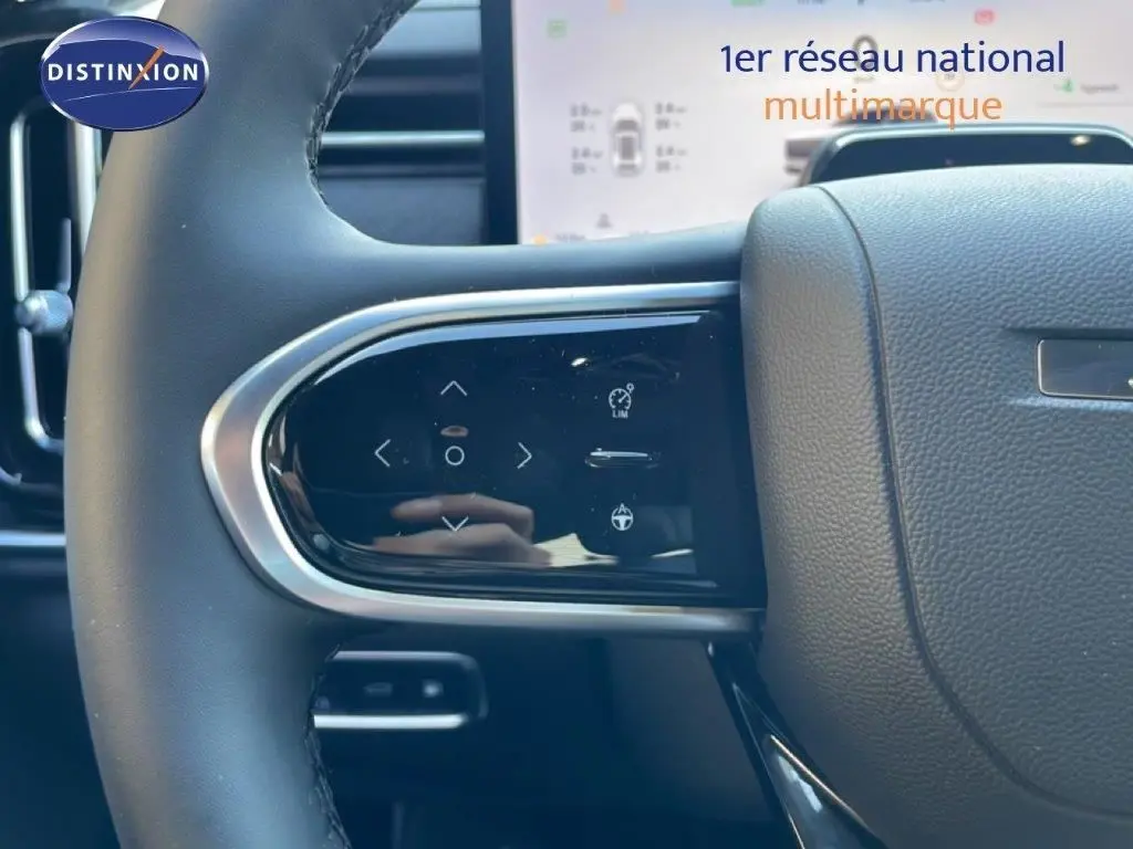 Gros plan sur les commandes tactiles au volant côté gauche du JAECOO J7 noir carbone, avec tableau de bord numérique en arrière-plan.