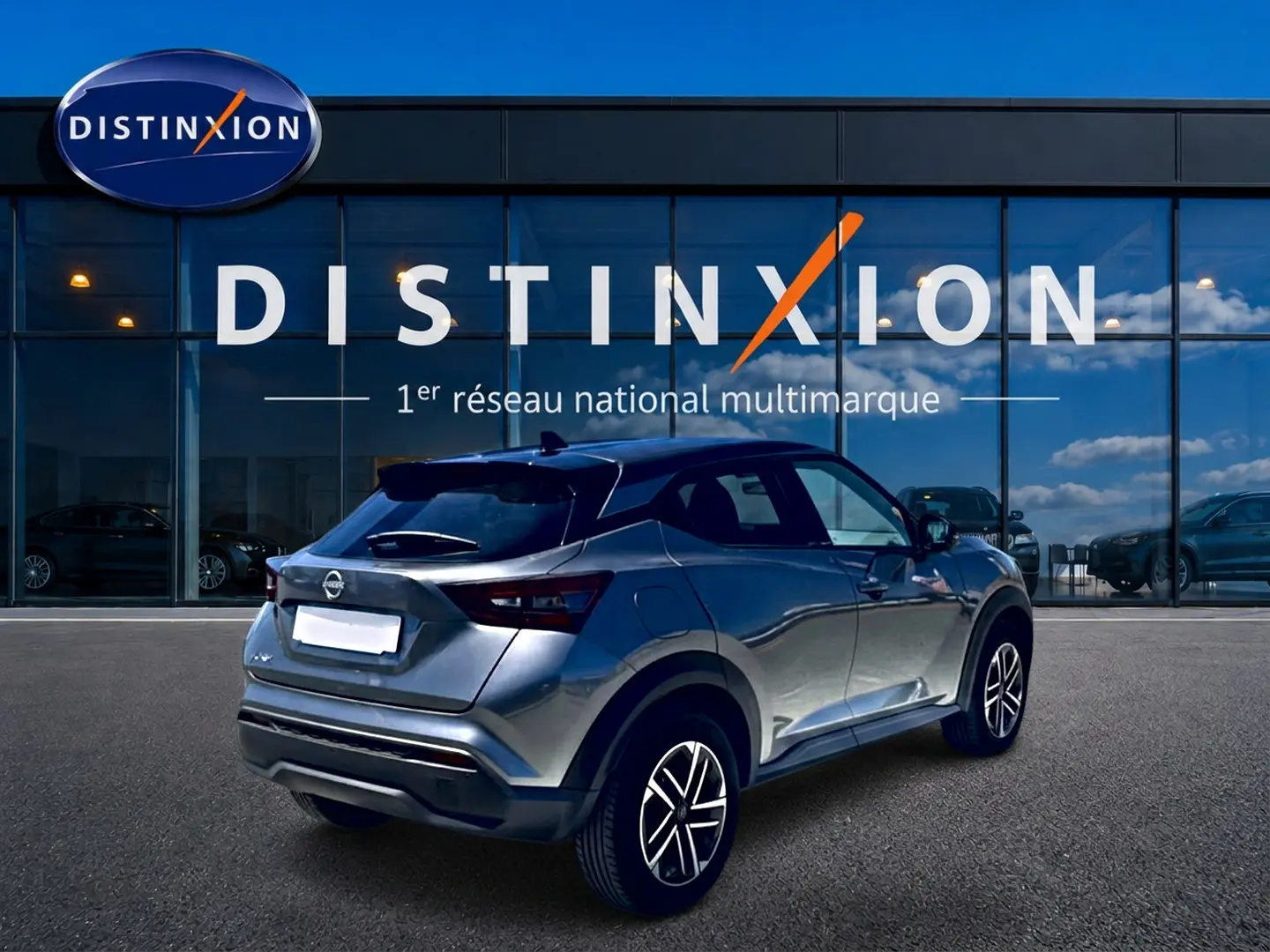 Nissan Juke gris 3/4 arrière droit, avec jantes alu et toit noir, devant une vitrine Distinxion.