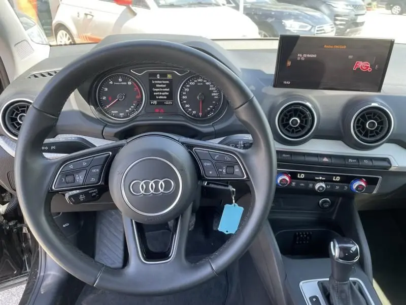Vue intérieure centrée sur le volant Audi Q2 2022 noir métal, tableau de bord et écran multimédia allumé.