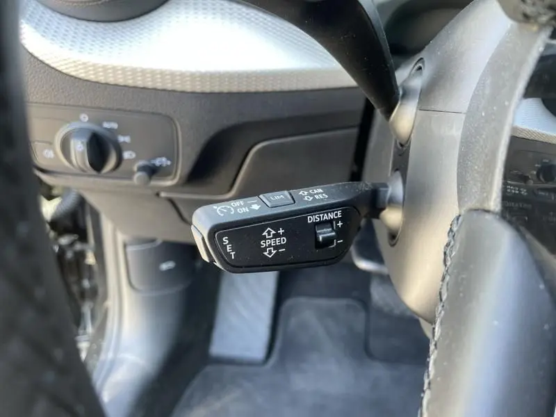 Gros plan sur la commande de régulateur de vitesse à gauche du volant dans l'Audi Q2 noir métal 2022.