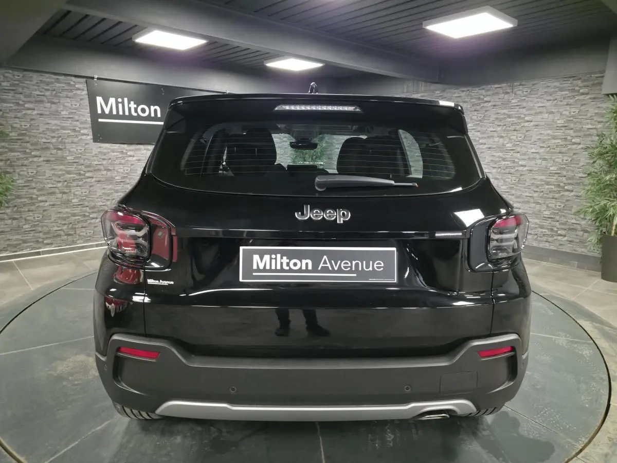 Vue arrière d'un Jeep Avenger noir avec feux arrière fumés et plaque Milton Avenue dans un showroom.
