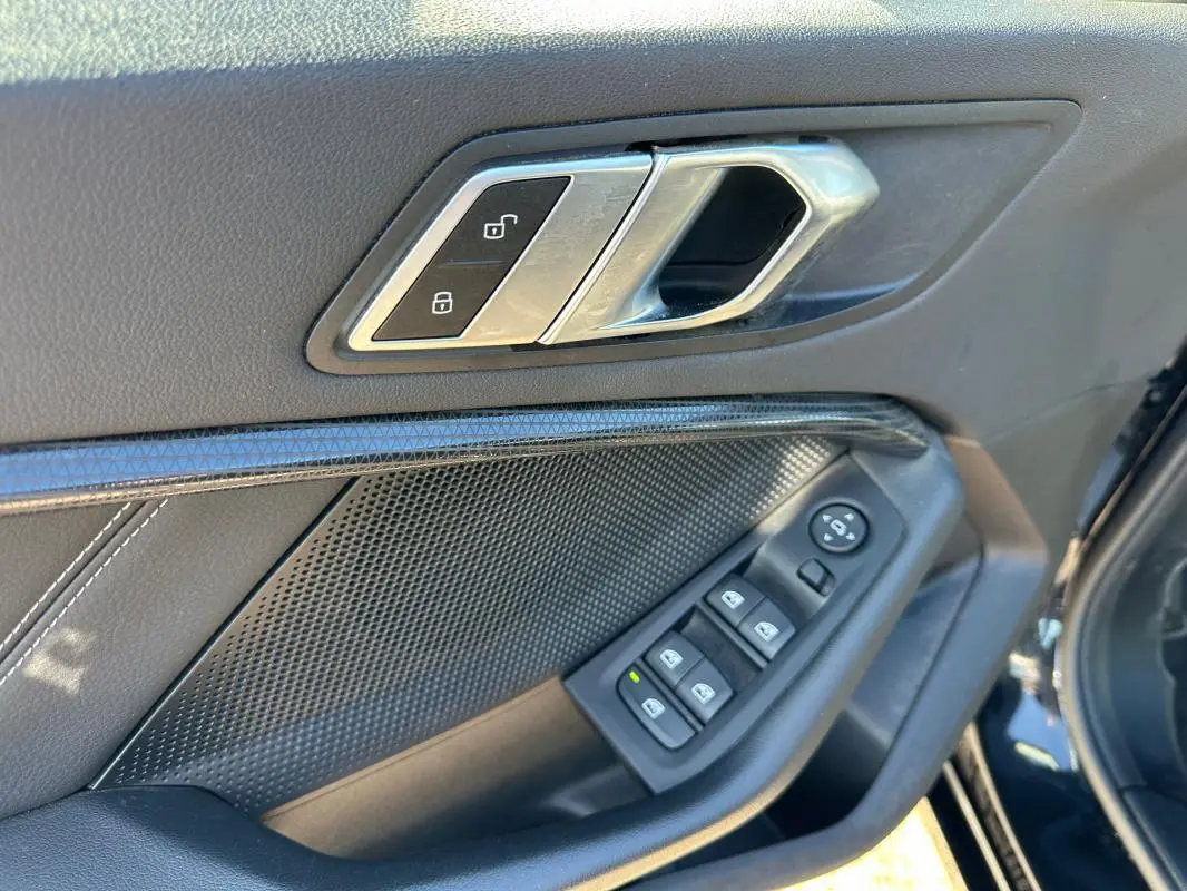 Poignée intérieure côté conducteur de BMW Série 1 noire, avec commandes des vitres et verrouillage centralisé.