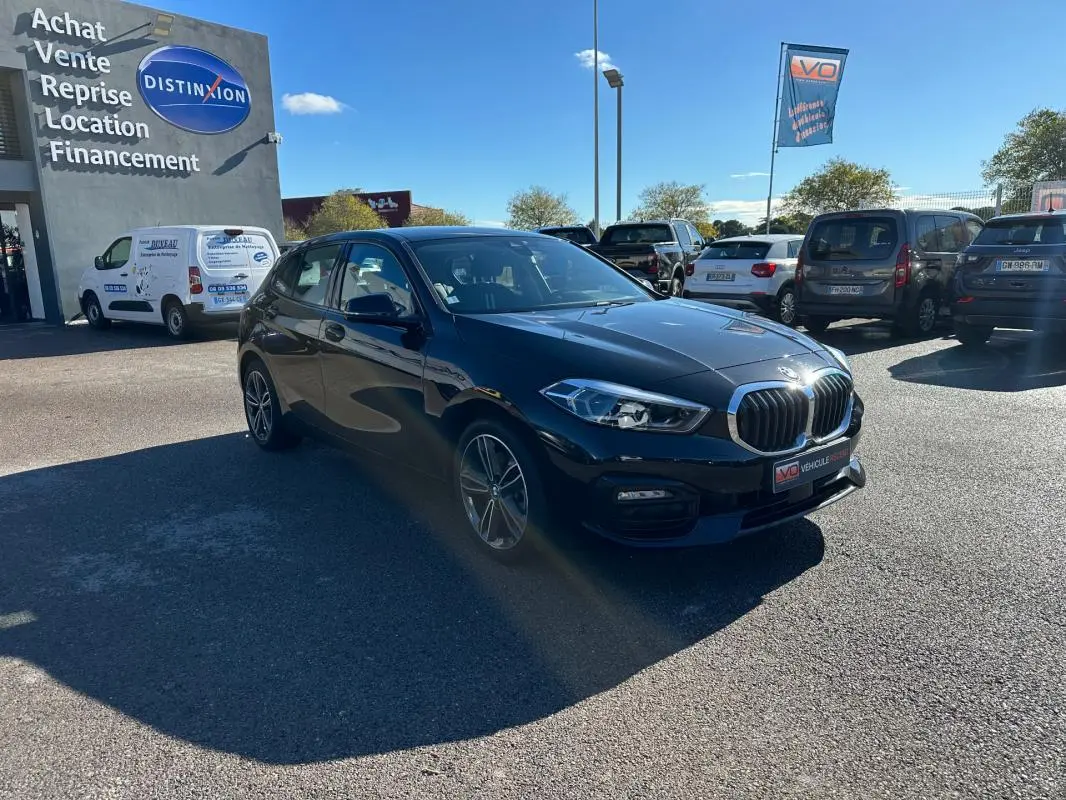 BMW Série 1 F40 118d noire vue 3/4 avant droit sur parking ensoleillé devant un garage Distinxion.