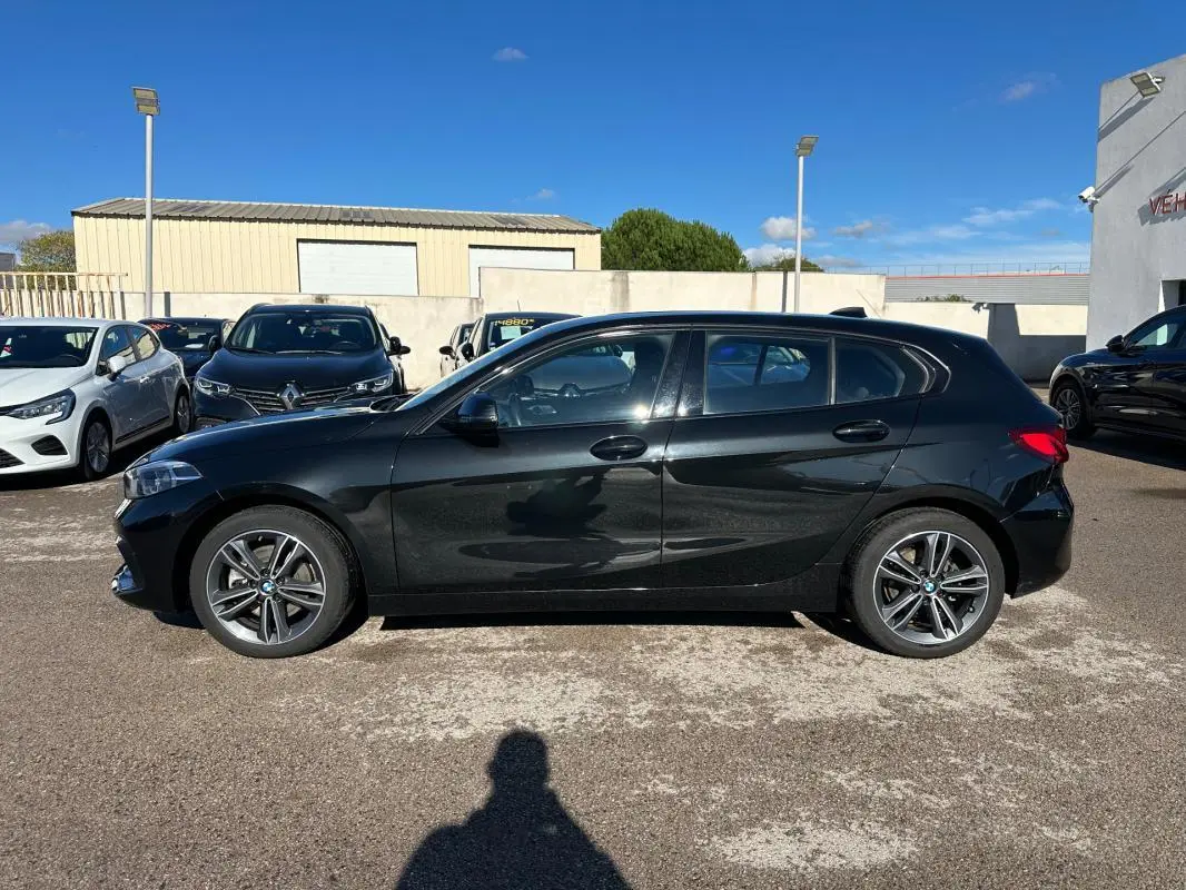 Profil côté gauche d'une BMW Série 1 F40 noire, avec jantes alliage 17 pouces, stationnée en extérieur au soleil.