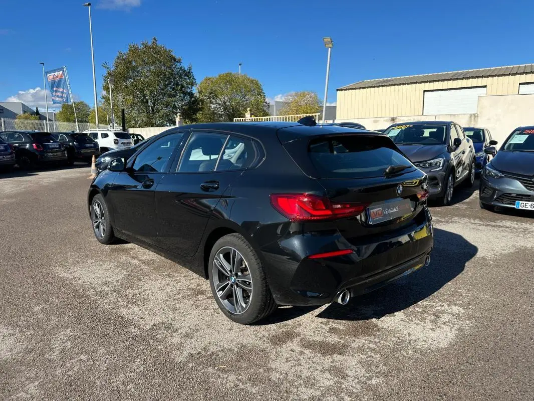 BMW Série 1 F40 118d noire vue en 3/4 arrière droit, avec jantes alliage 17 pouces et double sortie d'échappement chrome.