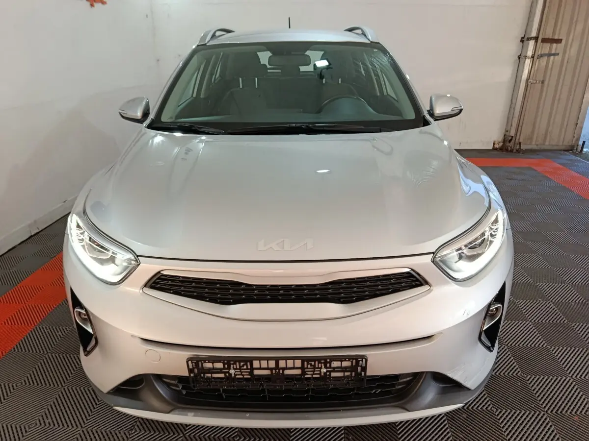 Vue avant d'un KIA Stonic gris clair 2022 avec phares allumés et calandre noire dans un garage.