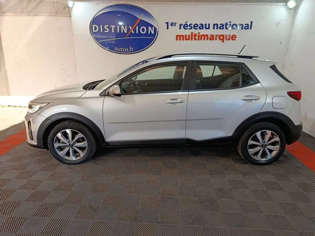 Vue de profil côté gauche d'un KIA Stonic gris clair 2022, avec jantes alliage et protections noires sur les passages de roues.