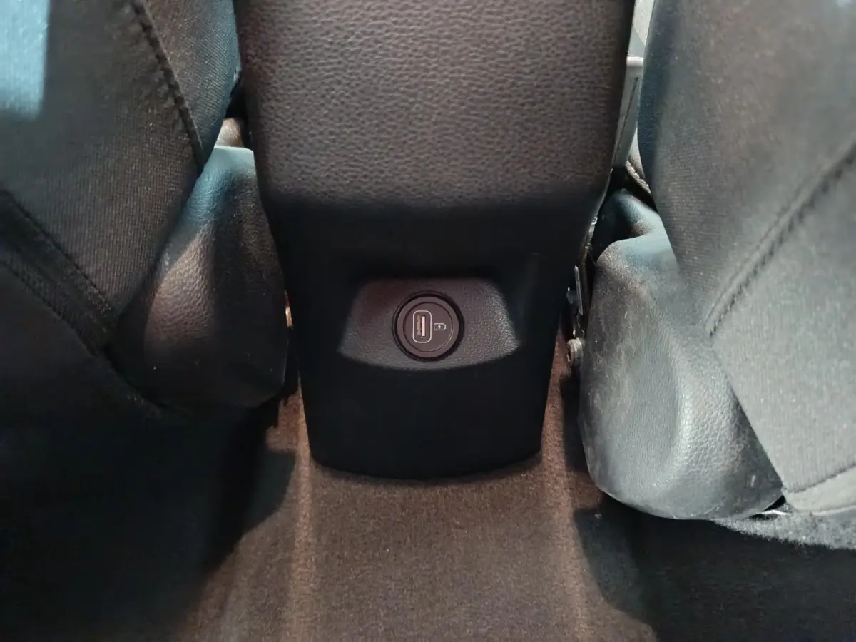 Prise USB arrière entre les sièges noirs du Kia Stonic 1.0 T-GDI 100 Urban gris clair, vue rapprochée du plancher.