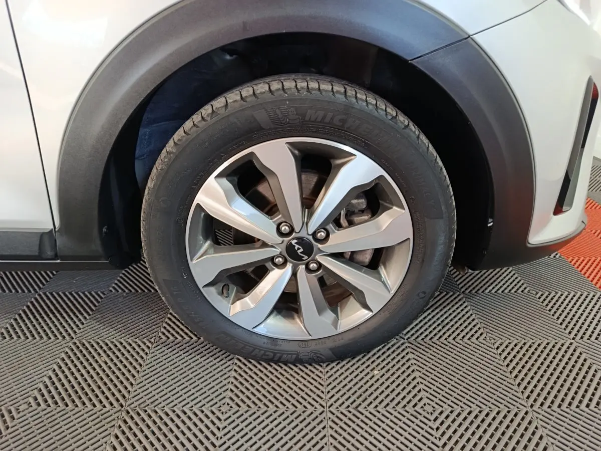 Gros plan sur la roue avant droite d'un KIA Stonic gris clair, avec jante alliage et logo KIA visible au centre.