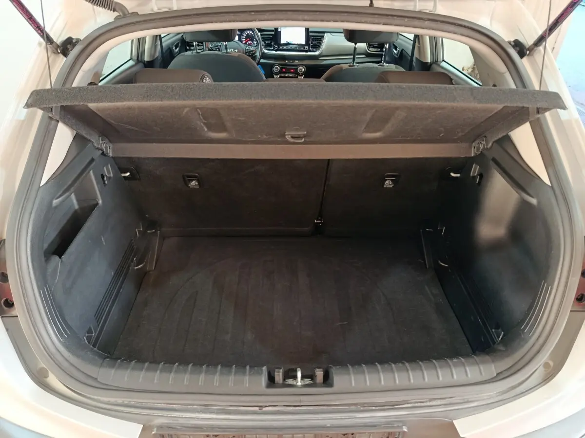 Coffre ouvert d'une KIA Stonic gris clair vue de l'arrière, montrant l'intérieur spacieux et la tablette de séparation.