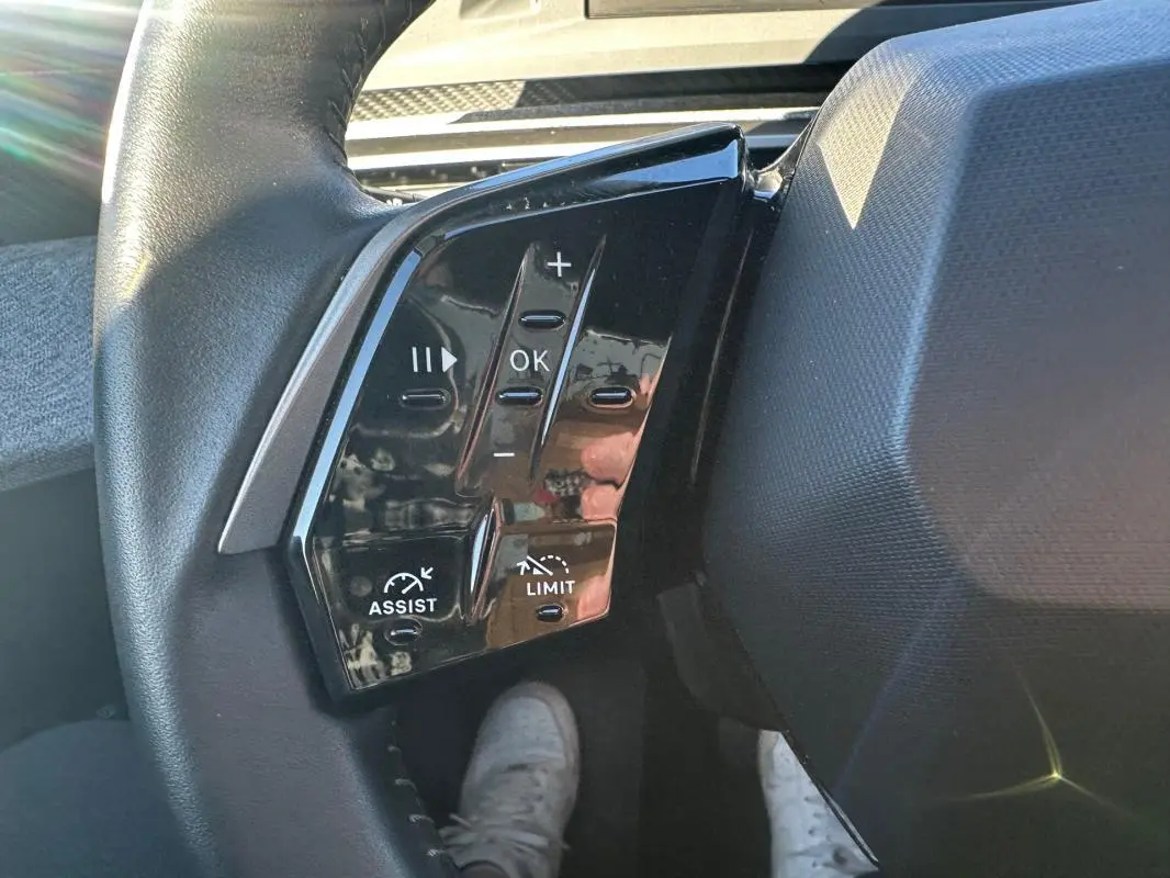 Gros plan sur les commandes noires au volant du Peugeot 3008 Hybrid blanc, avec boutons de réglage et assistance.